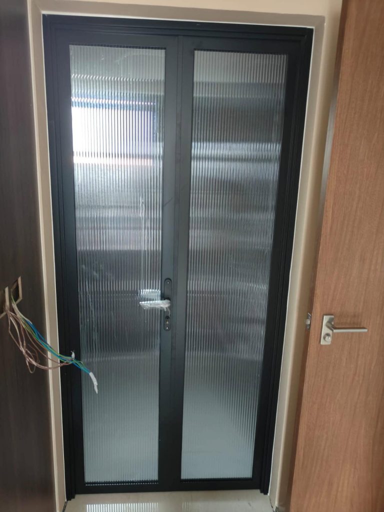 Front view of newly installed, double-swinging custom black aluminium fluted glass doors featuring a silver handle and textured glass panels.
