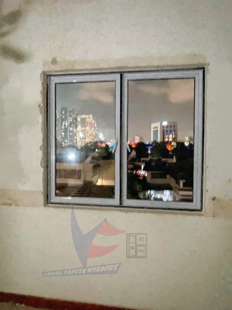 A recent project installation of a double-pane aluminum casement window. The clear glass provides a vibrant view of illuminated high-rise buildings against a night sky.