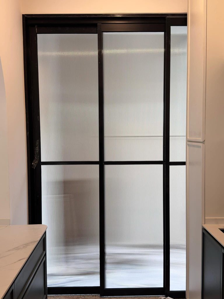 A sleek, black Modern aluminum sliding door with fluted glass installed between two kitchen counters to partition the living space.