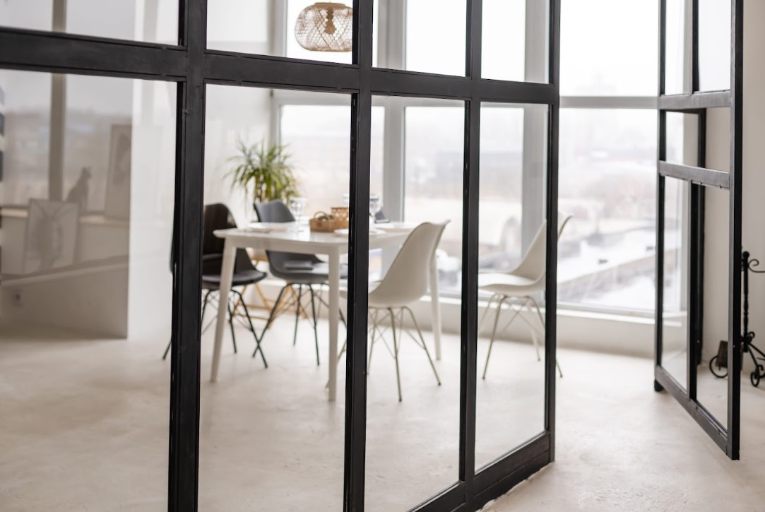 Modern interior with a white dining table and chairs, viewed through black aluminium-framed glass partition doors.