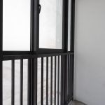 A close-up view of a modern black aluminium window frame and a matching black metal balcony railing against a plain white wall.
