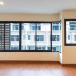 An empty room with wood laminate flooring and cream-colored walls, featuring two large black-framed windows with aluminium grilles