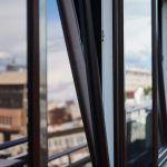 Open aluminium BTO window with slim black frames, providing natural ventilation and overlooking an urban residential view