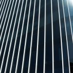 Modern glass building façade with vertical lines resembling an invisible grille design, showcasing a sleek and minimalist architectural appearance.
